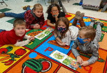 Students laying on a mat on the floor reading books as part of 'Partner Reading' learning