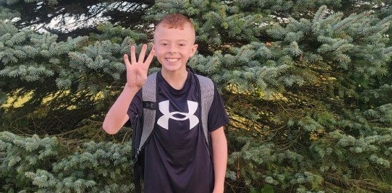 Student posing for the first day of school, holding up four fingers to represent 4th grade