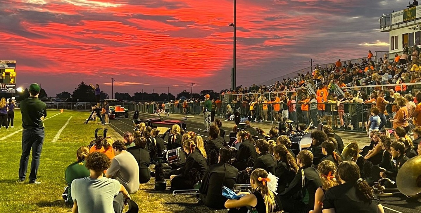 Beautiful orange sky at a football game with the band on the sidelines and the fans in the stands